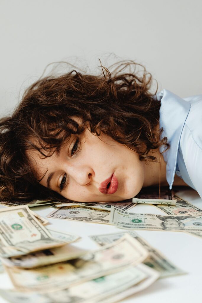 Close-up of a curly-haired woman resting on US dollar bills, conveying financial contemplation.